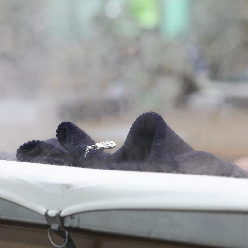 Dampf steigt an einem dunklen RYMHART-Gestrick auf dem Dämpftisch auf